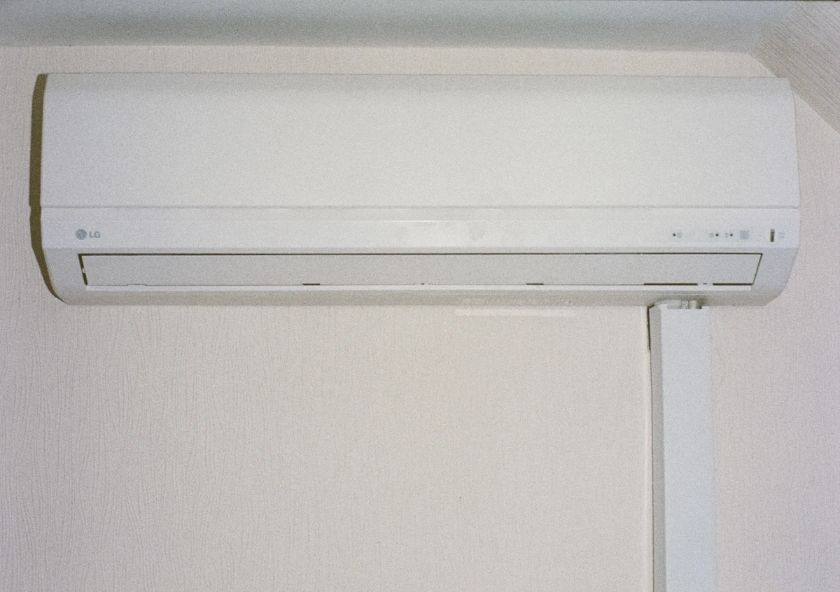 White wall-mounted split air conditioner indoor unit on a cream wall with a cable duct running down beside it