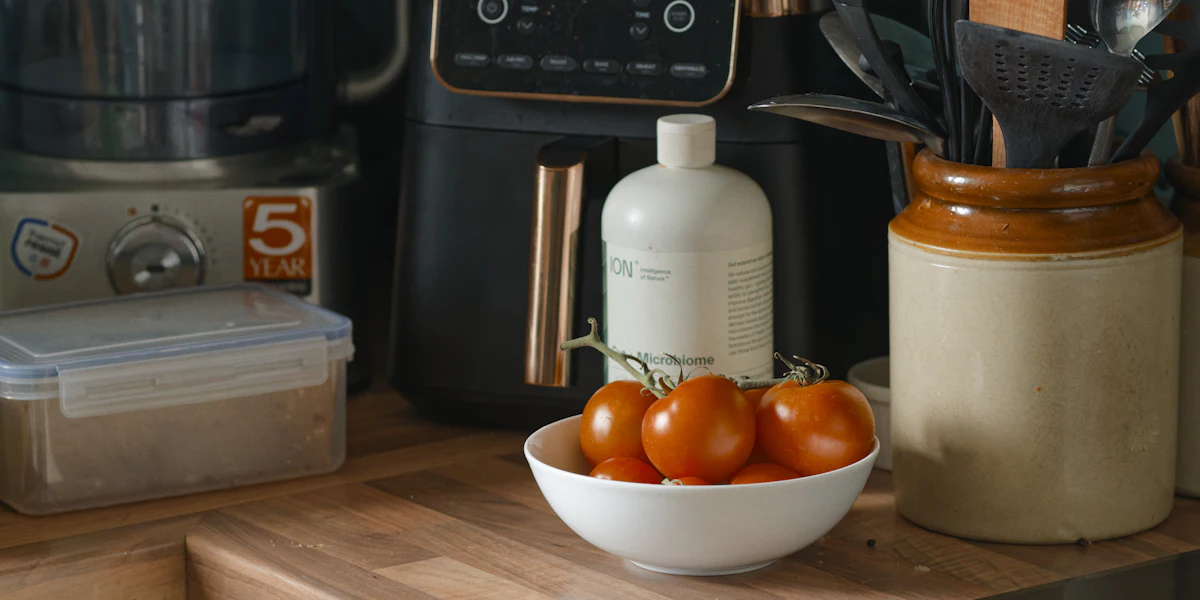 Black countertop air fryer behind a bowl of tomatoes and a ceramic jar of kitchen utensils