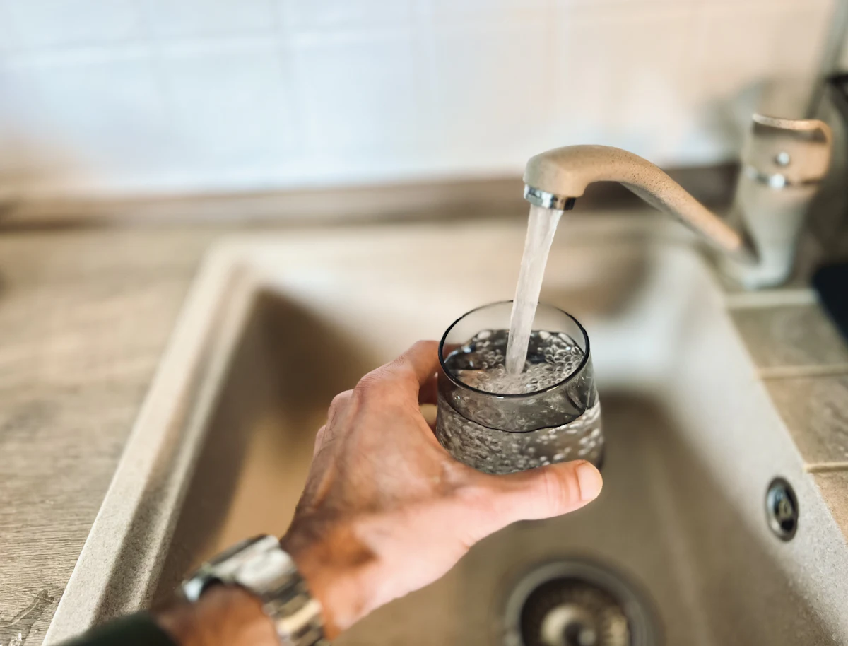Hand holding a glass under a kitchen tap while clear water pours into it over a sink